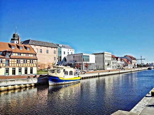 a boat is docked in a river next to buildings at Ferienwohnung Am Ueckerpark in Ueckermünde