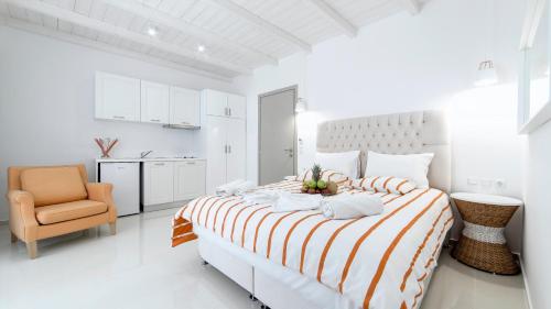 a white bedroom with a large bed and a chair at Liberte Maisonettes in Parga