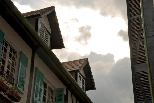 two buildings with green shutters and a cloudy sky at Colmar Tropicale in Bukit Tinggi
