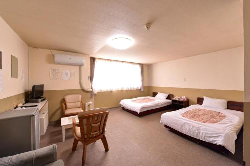 a room with two beds and a desk and a television at Hotel Million in Muroran