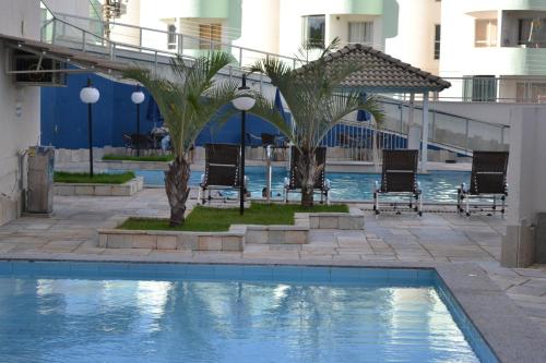 una piscina con palmeras y sillas junto a un edificio en Cézar's Park Flat, en Caldas Novas
