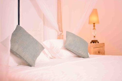 two pillows on a white bed with a lamp at Handun Villas in Talalla