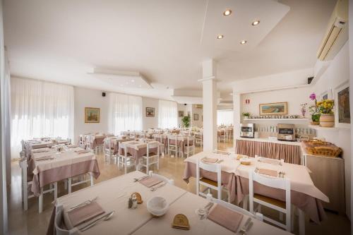 uma sala de jantar com mesas brancas e cadeiras brancas em Hotel Augusta em Caorle