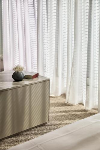 a bedroom with white curtains and a table with a book at The Mandala Berlin, a Member of Design Hotels in Berlin