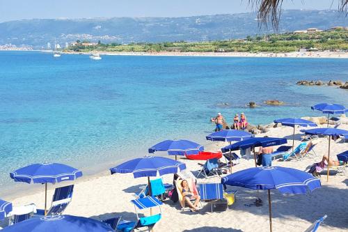 a beach with blue umbrellas and people on the beach at Residence Albatros in Briatico