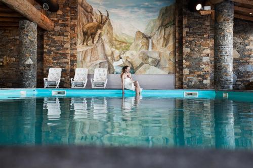 une femme assise à l'eau dans une piscine dans l'établissement Residence Les Hauts Bois - maeva Home, à Aime La Plagne
