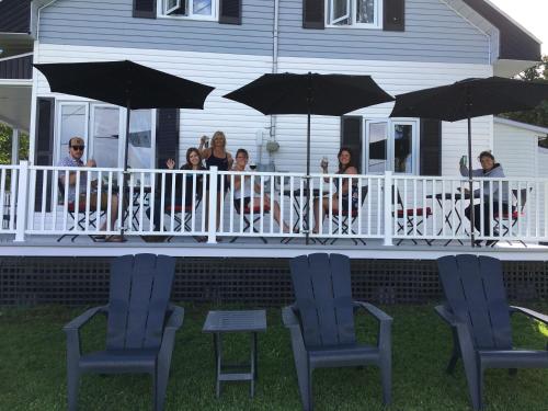 eine Gruppe von Menschen, die auf einer Veranda mit Sonnenschirmen sitzen in der Unterkunft Gîte de la colline in Baie-Sainte-Catherine