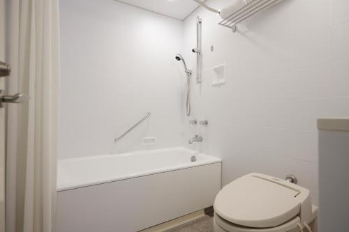 a white bathroom with a toilet and a bath tub at Hotel Nikko Kanazawa in Kanazawa