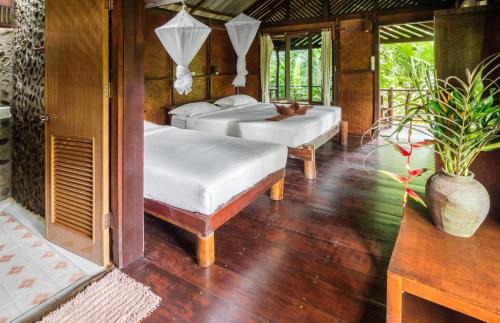 two beds in a room with wood floors and windows at Khao Sok Riverside Cottages in Khao Sok