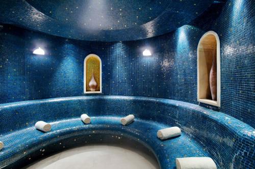 a blue tiled bathroom with a bath tub with two windows at Raffles Makkah Palace in Makkah