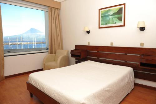 um quarto com uma cama, uma cadeira e uma janela em Hotel São Francisco em Horta