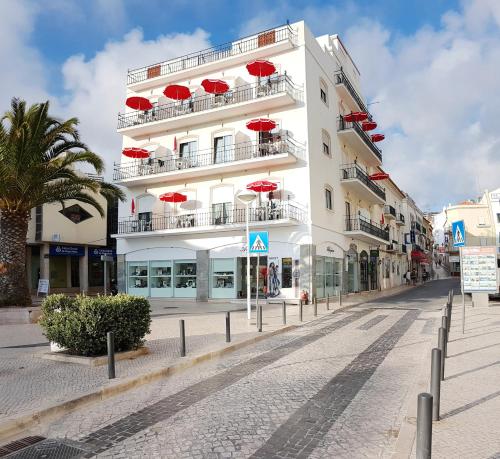 a white building with red umbrellas on a street at Solar dos Carvalhos - Apartamentos de Turismo in Nazaré