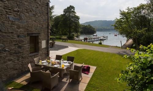 a table and chairs on a lawn next to the water at Hill Of Oaks in Windermere