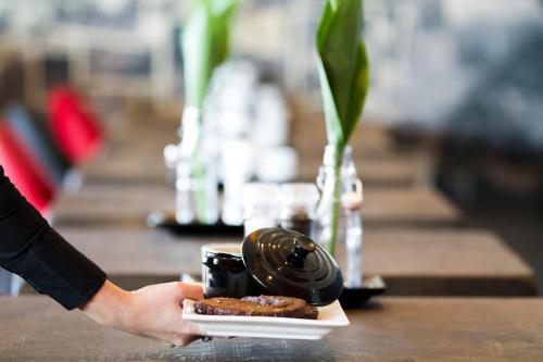 a person holding a plate with a coffee cup and donuts at Bastion Hotel Tilburg in Tilburg