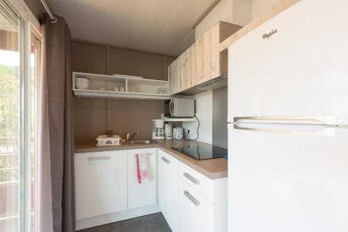 a small kitchen with white cabinets and a refrigerator at Domaine Chalets Larlapean in Saint-Martin-dʼArrossa