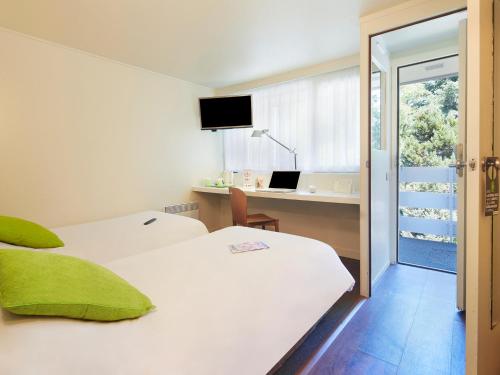 a room with two beds and a desk with a laptop at Campanile Orleans - La Source in Orléans