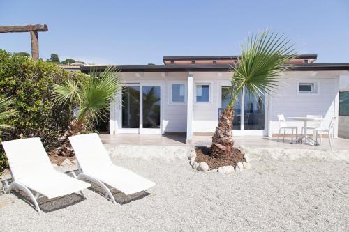 two white chairs and a palm tree in front of a house at Marinella Beach Apartments - On The Beach - Private Free Parking in Capo Vaticano