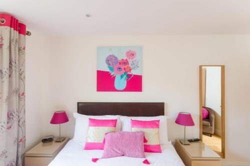 1 dormitorio con cama con almohadas rosas y espejo en 2 Suffolk Cottage, Knodishall, en Aldringham