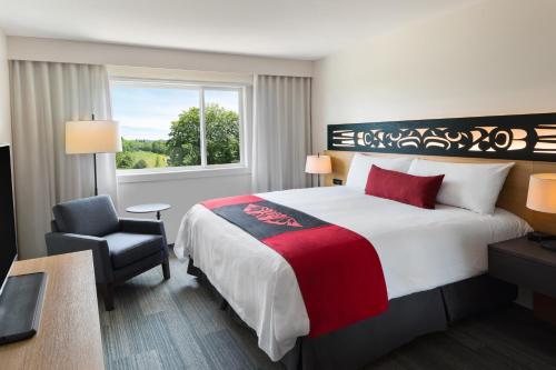 Habitación de hotel con cama, silla y ventana en Kwa'lilas Hotel en Port Hardy