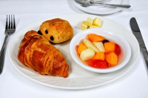 a plate of food with a croissant and a bowl of fruit at Ermitage Saint-Antoine in Lac-Bouchette