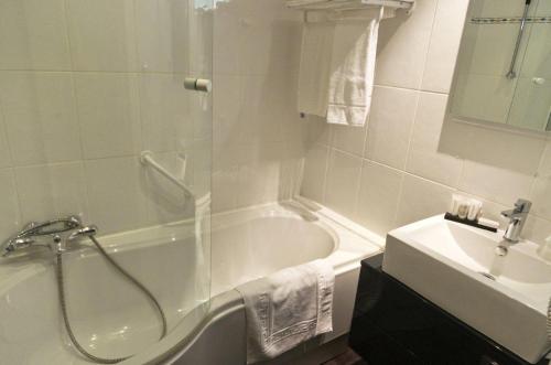 a white bathroom with a tub and a sink at Logis Hôtel Les Tuileries in Féy