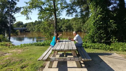 a man and woman sitting at a picnic table next to a river at Red Carpet Inn Kinston in Kinston