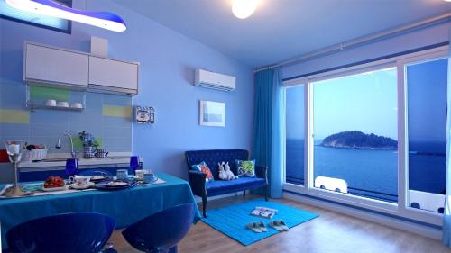 ein blaues Wohnzimmer mit einem Tisch und einem großen Fenster in der Unterkunft Blue & White Pension in Namhae