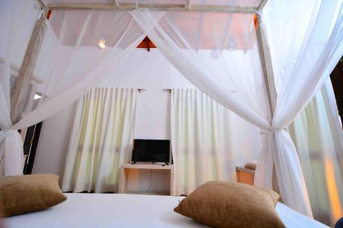 a bedroom with a bed with curtains and a television at Handun Villas in Talalla