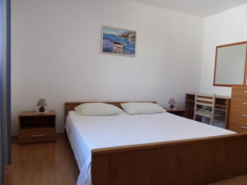 una camera da letto con un grande letto con lenzuola bianche e pavimenti in legno di Apartmani Lili a Mali Lošinj (Lussinpiccolo)