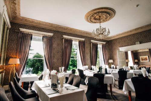 a restaurant with white tables and chairs and a chandelier at Belmont House Hotel in Banbridge