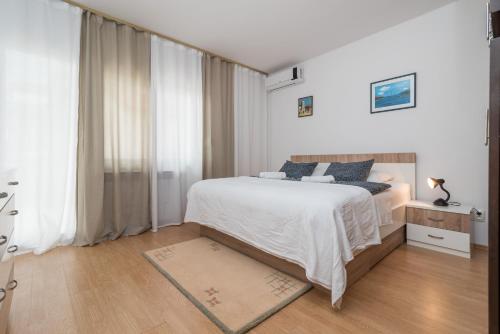 a white bedroom with a bed and a large window at Apartments Vojin in Trogir