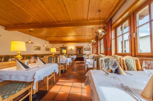 een restaurant met witte tafels, stoelen en ramen bij Hotel Hell in Monguelfo