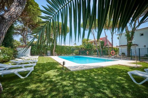 a swimming pool with lawn chairs and a palm tree at Casagrande - La Barrosa in Chiclana de la Frontera