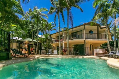 a swimming pool in front of a house with palm trees at Beaches Apartments Byron Bay in Byron Bay