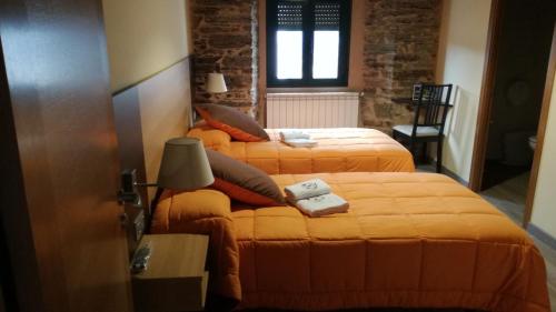 two beds in a hotel room with orange sheets at Albergue Pension Porta Santa in Baleira
