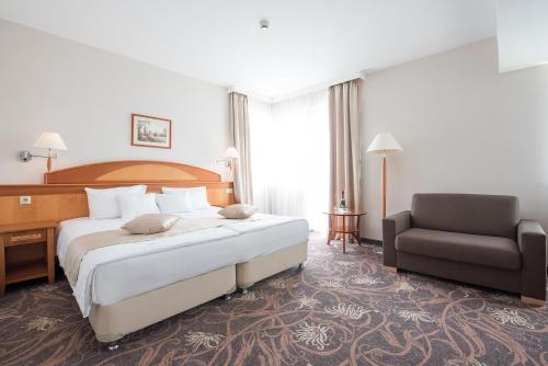 シャールヴァールにあるVitalmed Hotel Sárvárの大きなベッドと椅子が備わるホテルルームです。