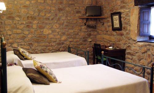 a room with three beds and a tv on a stone wall at Posada Rural Ochohermanas in Las Fraguas