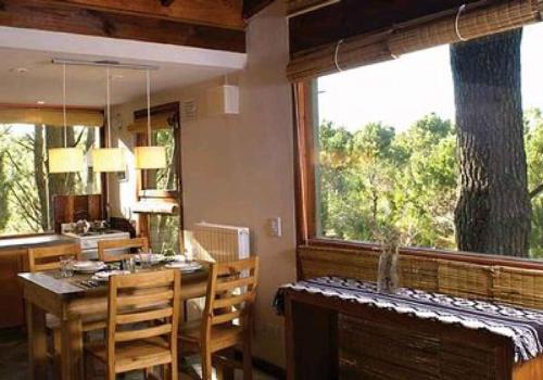 comedor con mesa y ventana grande en Altos Medanos Cabañas & Club de Bosque en Mar de las Pampas