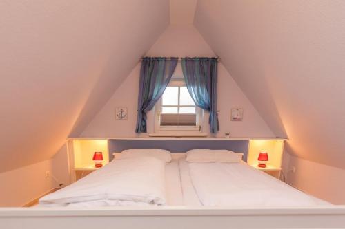 ein weißes Bett mit einem Fenster im Dachgeschoss in der Unterkunft Haus Anke, Wohnung Muschelsucher, Westerlandstr. 37 in Wenningstedt-Braderup