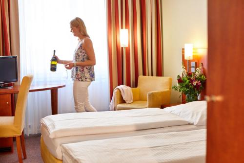 una mujer parada en una habitación de hotel con una botella de vino en Hotel Concorde en Múnich