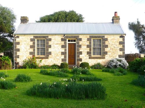 a brick house with a grass yard in front of it at Cherry Plum Cottages in Port Fairy