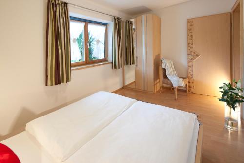 a bedroom with a white bed with a chair and a window at Appartementhaus Charisma in Fieberbrunn