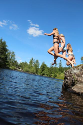 two girls jumping off a rock into a body of water at Lövås Gård Koppera in Charlottenberg
