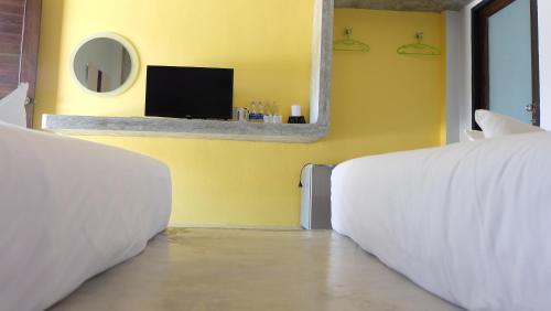 une chambre avec deux lits et une télévision sur un mur jaune dans l'établissement Lullaby Boutique Resort, à Thap Sakae