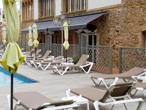 a row of lounge chairs and umbrellas next to a pool at Hotel Castell Blanc in Empuriabrava