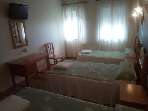 a room with three beds and a table and a television at Hotel Restaurante Las Camelias in Jarrio