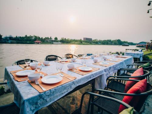 a long table with plates and wine glasses on the water at Good Times Resort Kanchanaburi in Kanchanaburi