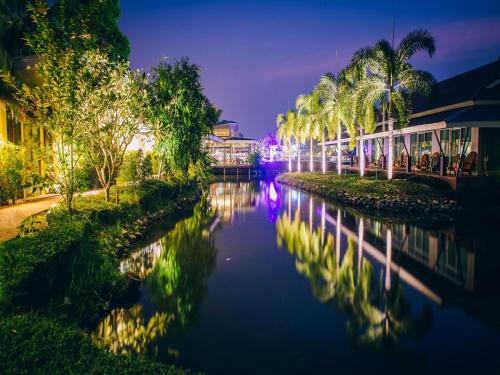 Good Times Resort Kanchanaburi في مدينة كانشانابوري: نهر فيه نخل ومباني بالليل