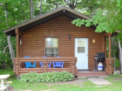 Cabaña de madera con 2 sillas y puerta blanca en Adventures East Cottages and Campground, en Baddeck Inlet