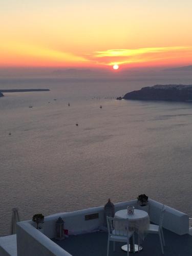 a sunset over the ocean with a table and chairs at Caldera's Majesty in Imerovigli